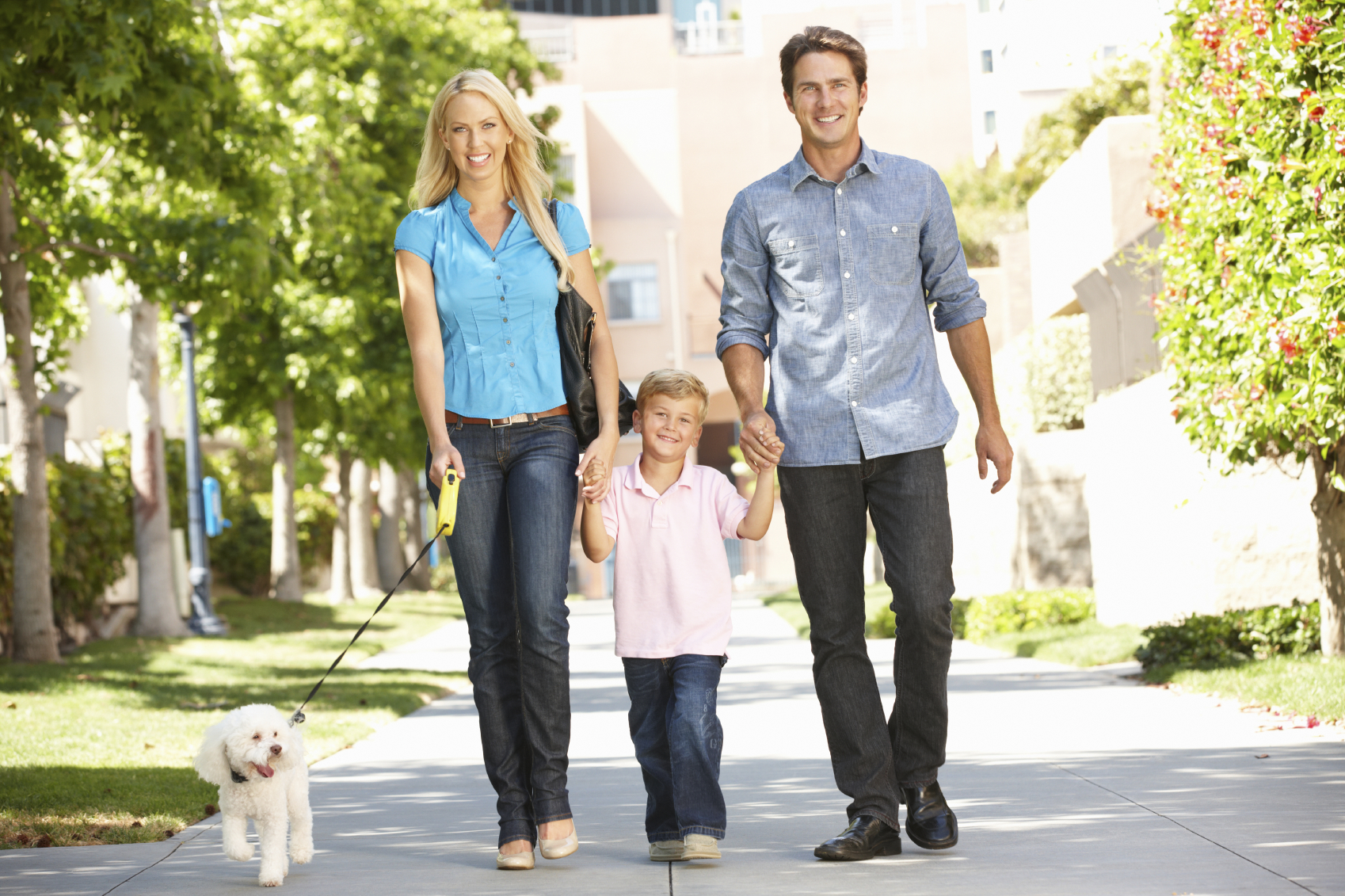 stock photo of two parents and a child, walking a dog together