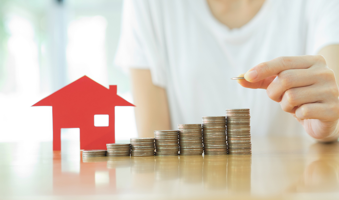 Stock photo of coins stacked like a bar chart, next to a miniature house