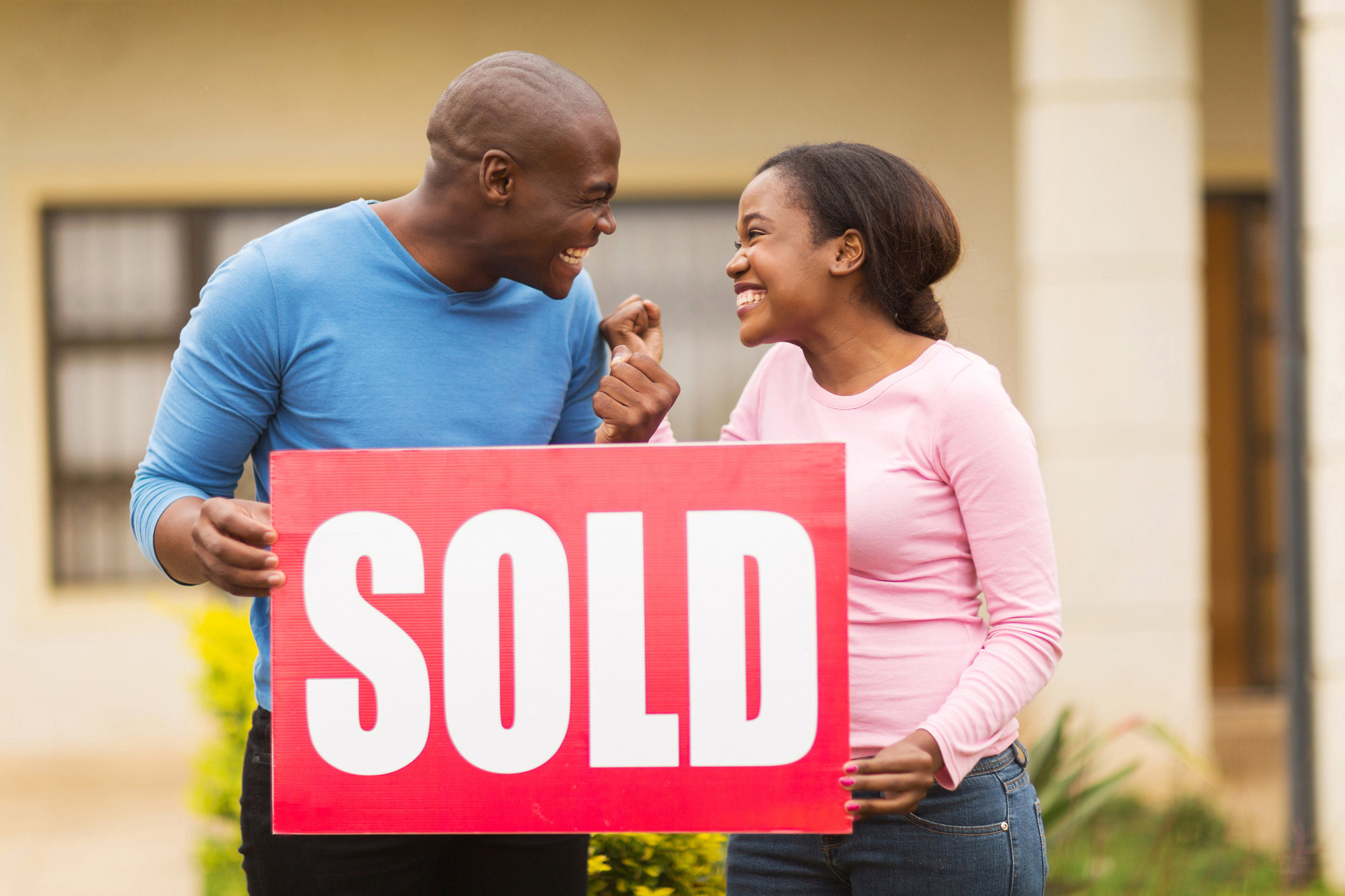 Stock photo of a couple behind a sold sign in a yard