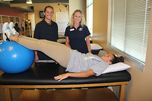 Two students guide a patient through physical therapy drills