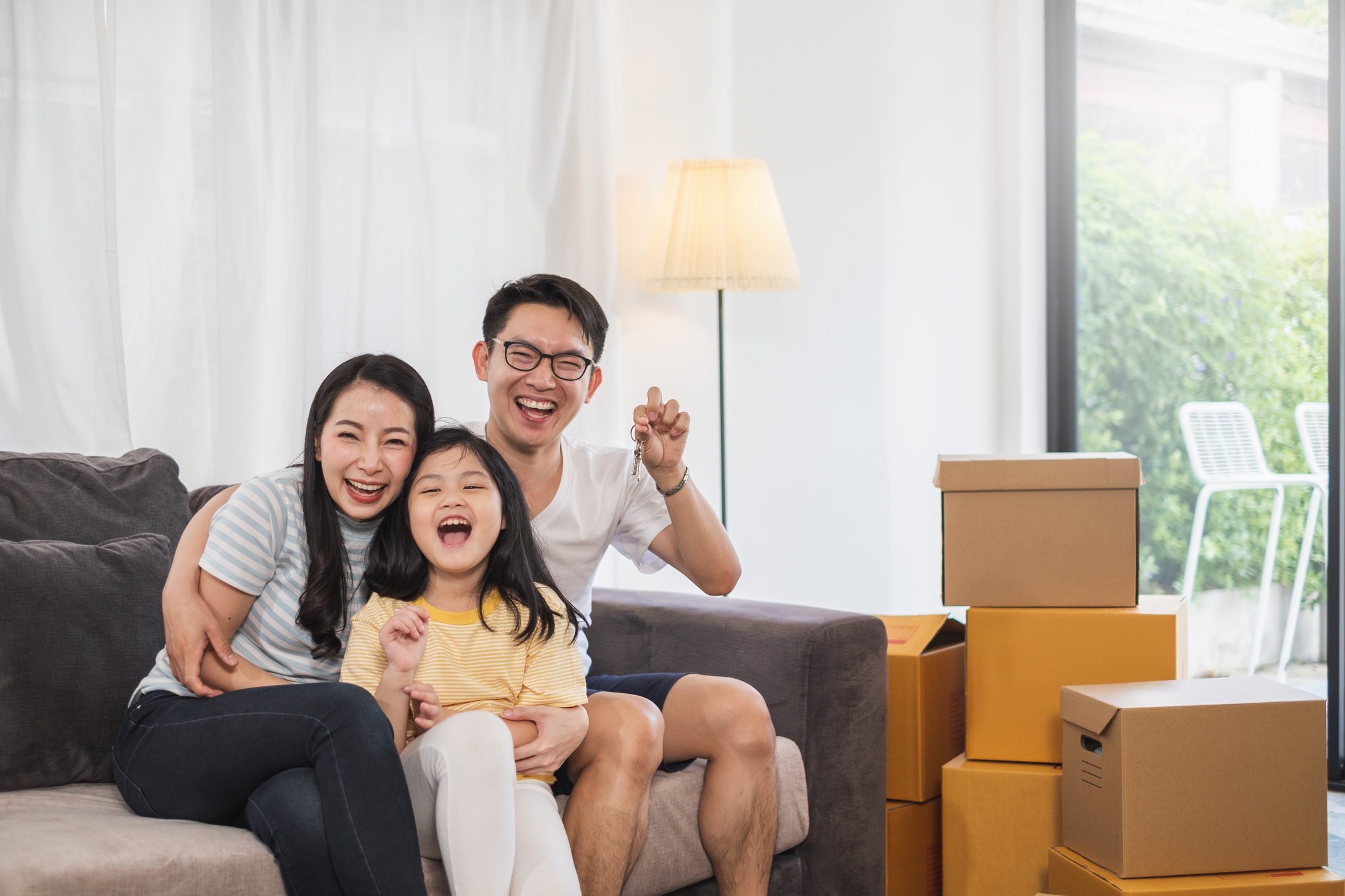 stock photo of family in living room surrounded by moving boxes and holding up keys