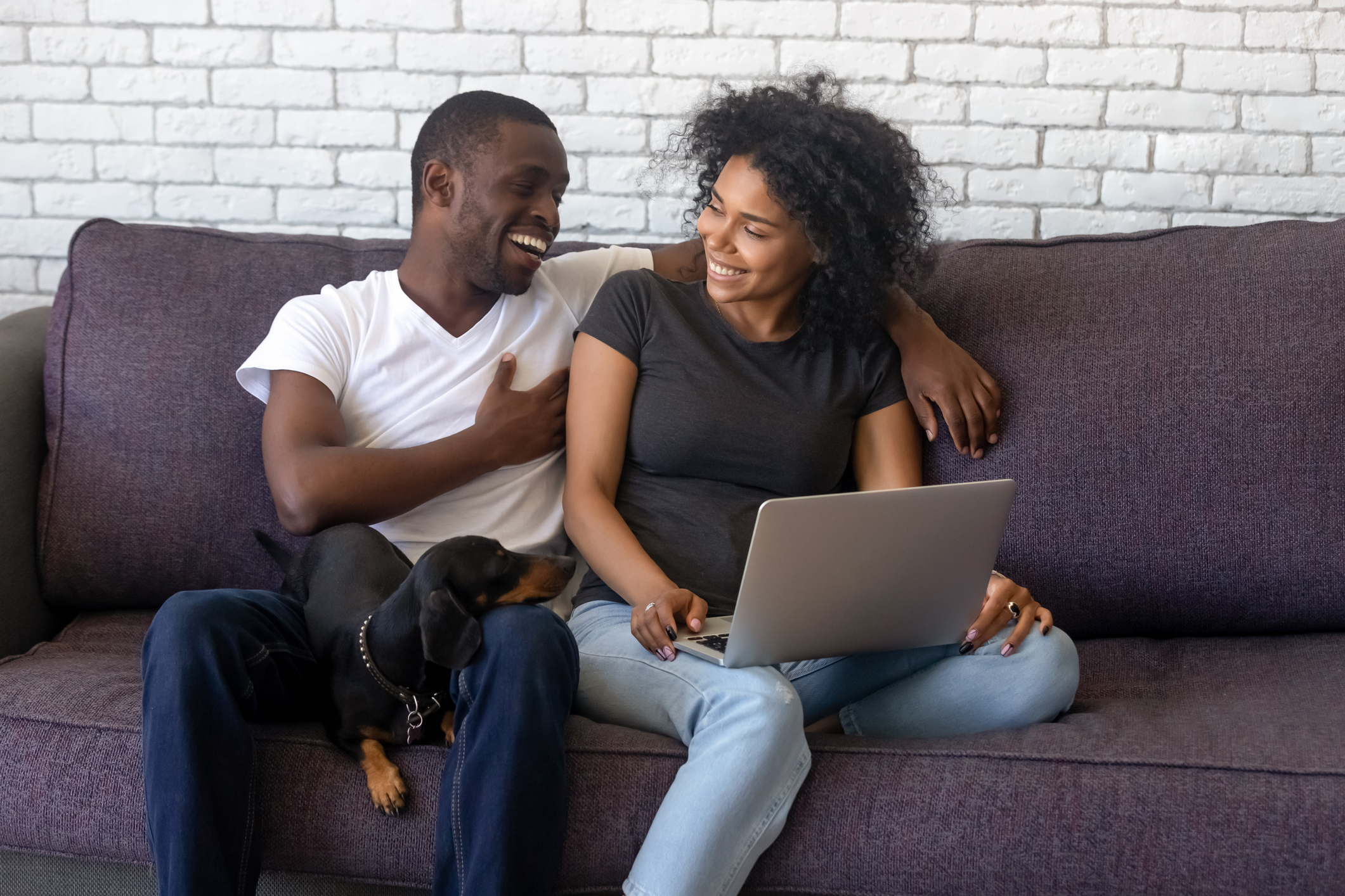 man and woman sitting on sofa looking at laptop and smiling