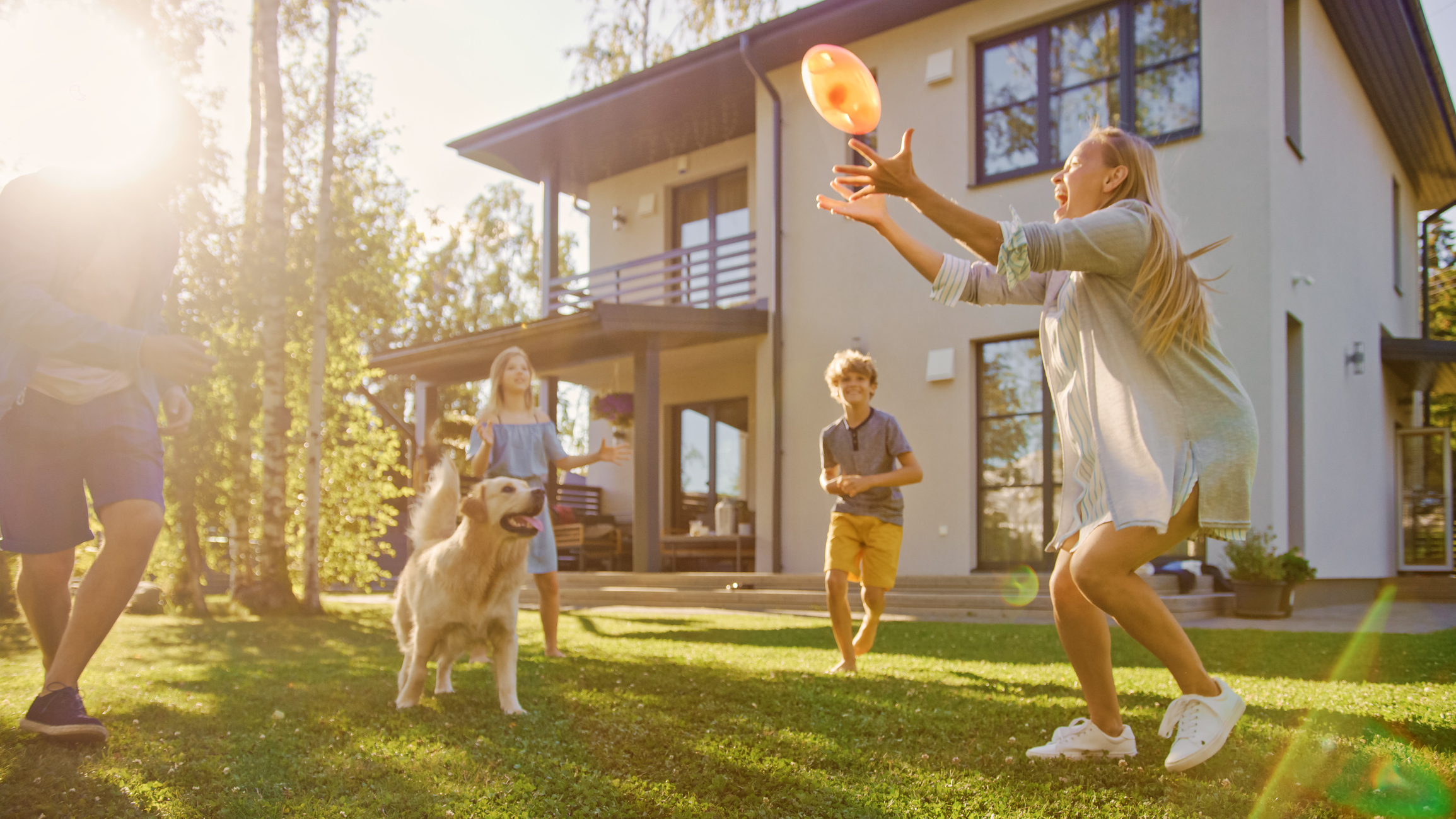 Stock photo of family and dog outside home playing frisbee