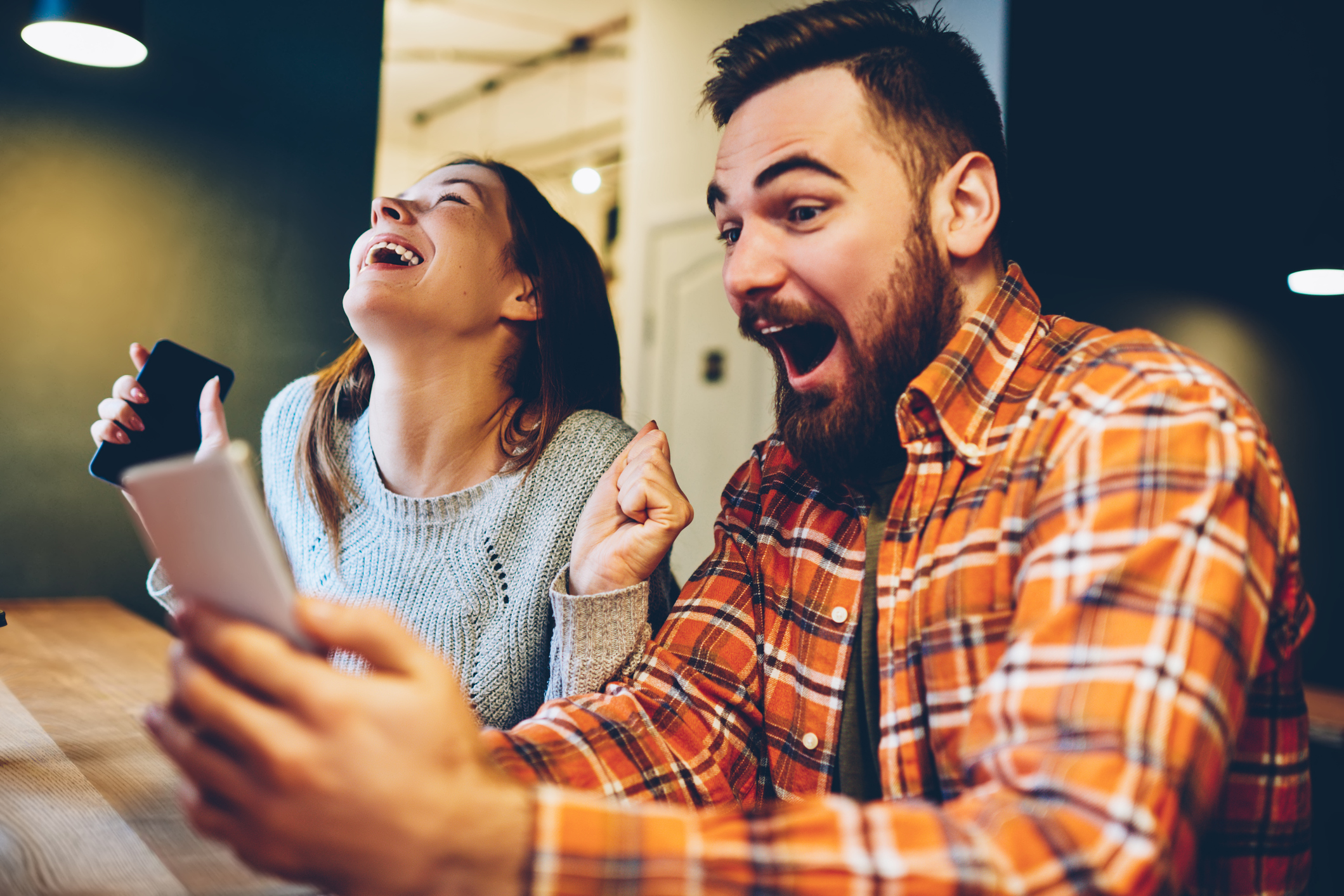 Stock image of a man and woman sitting together and laughing while looking at their cell phone screens.