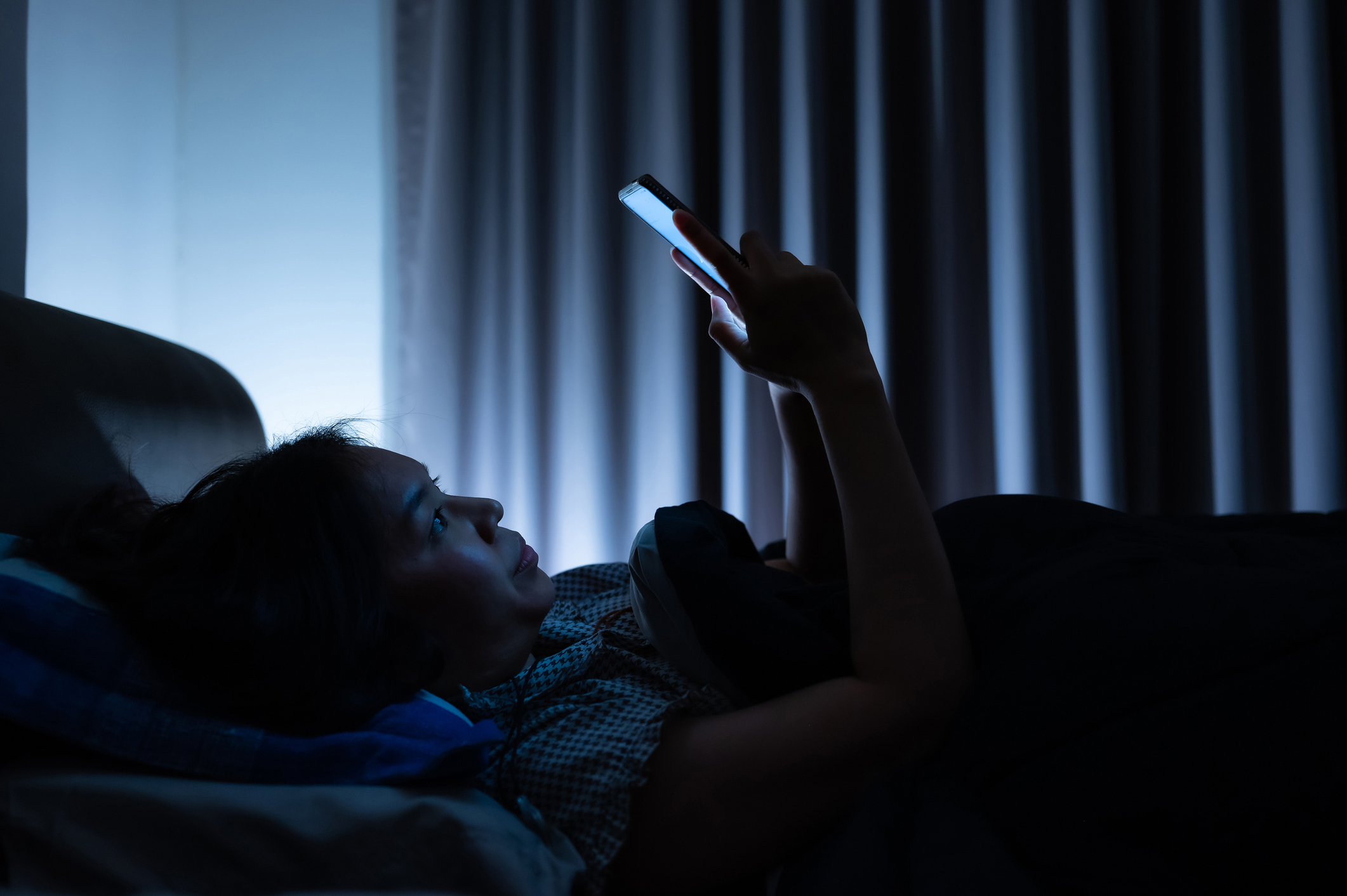 Stock image of a person lying in bed with the lights off and looking at a bright cell phone screen