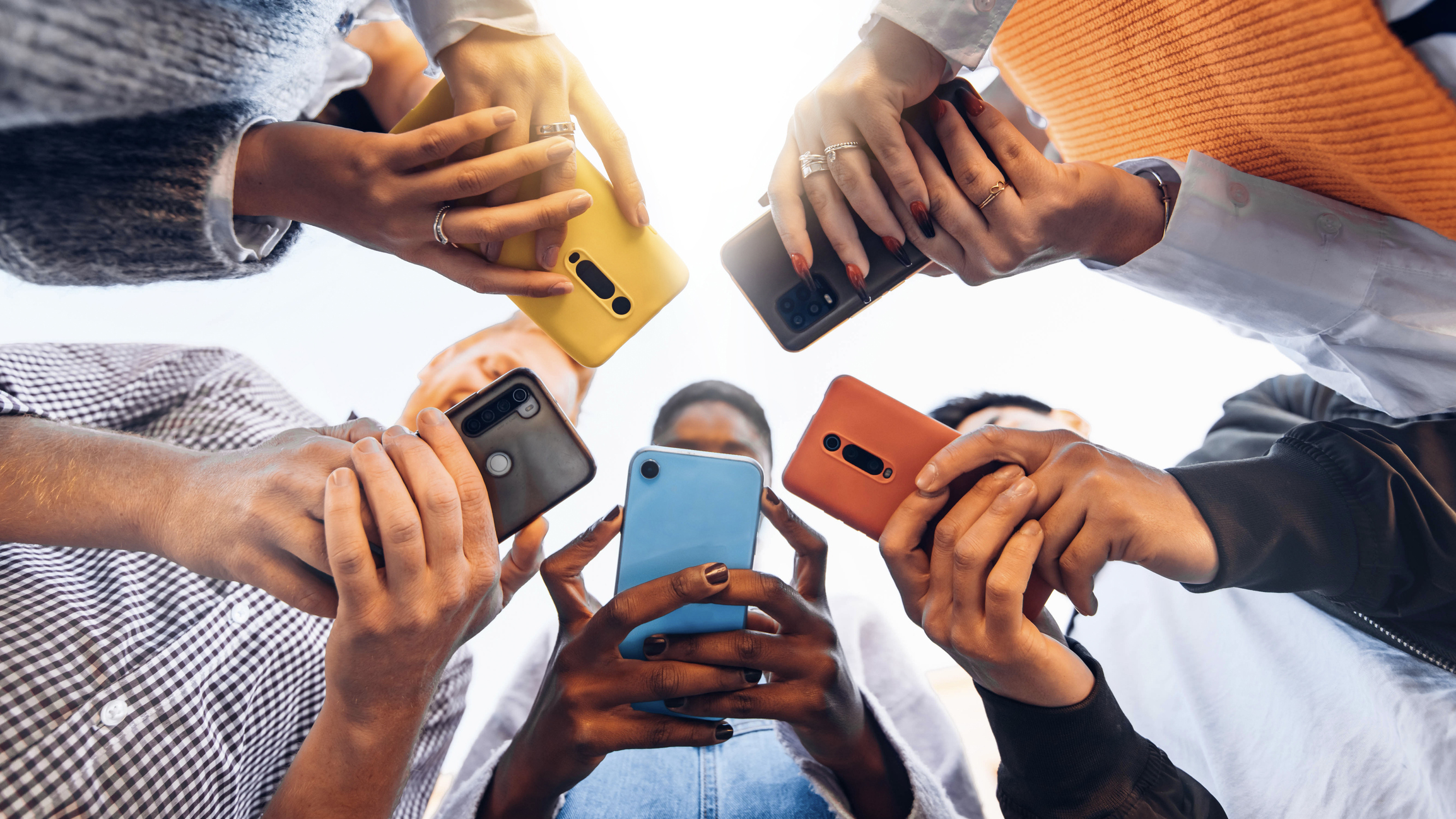 Stock image looking upward through hands of five individuals looking at and using their cell phones in a circle